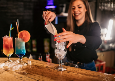 ragazza sorridente che prova a mettere il ghiaccio in un bicchiere durante un corso da barman organizzato da Studio Aschei